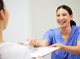 Dental assistant smiling while handing patient form
        